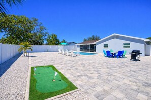 Un patio trasero con piscina, mobiliario de exterior y un pequeño campo de práctica de golf.
