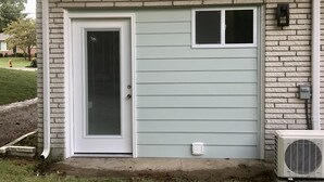 Una casa con puerta principal, una ventana pequeña y un equipo de aire acondicionado.
