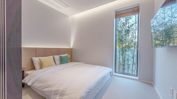 Un dormitorio moderno con una cama grande, cabecera de madera y vista a bambú a través de una ventana.