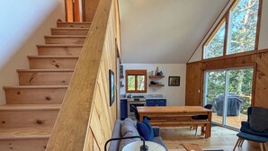 Un interior moderno con una escalera de madera, un comedor y grandes ventanales.