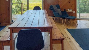 Interior de madera con una mesa y sillas, ventanas amplias y vista a la vegetación.