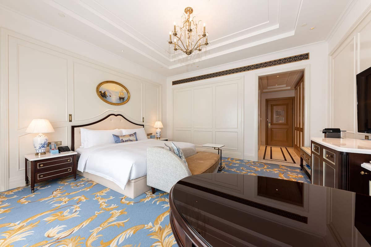 A hotel room with a large bed, a desk, a television, and a chandelier.