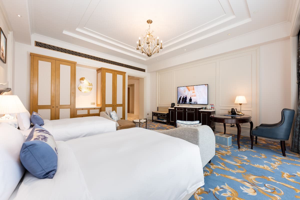 A hotel room with two large beds, a television, a desk, and a chair.