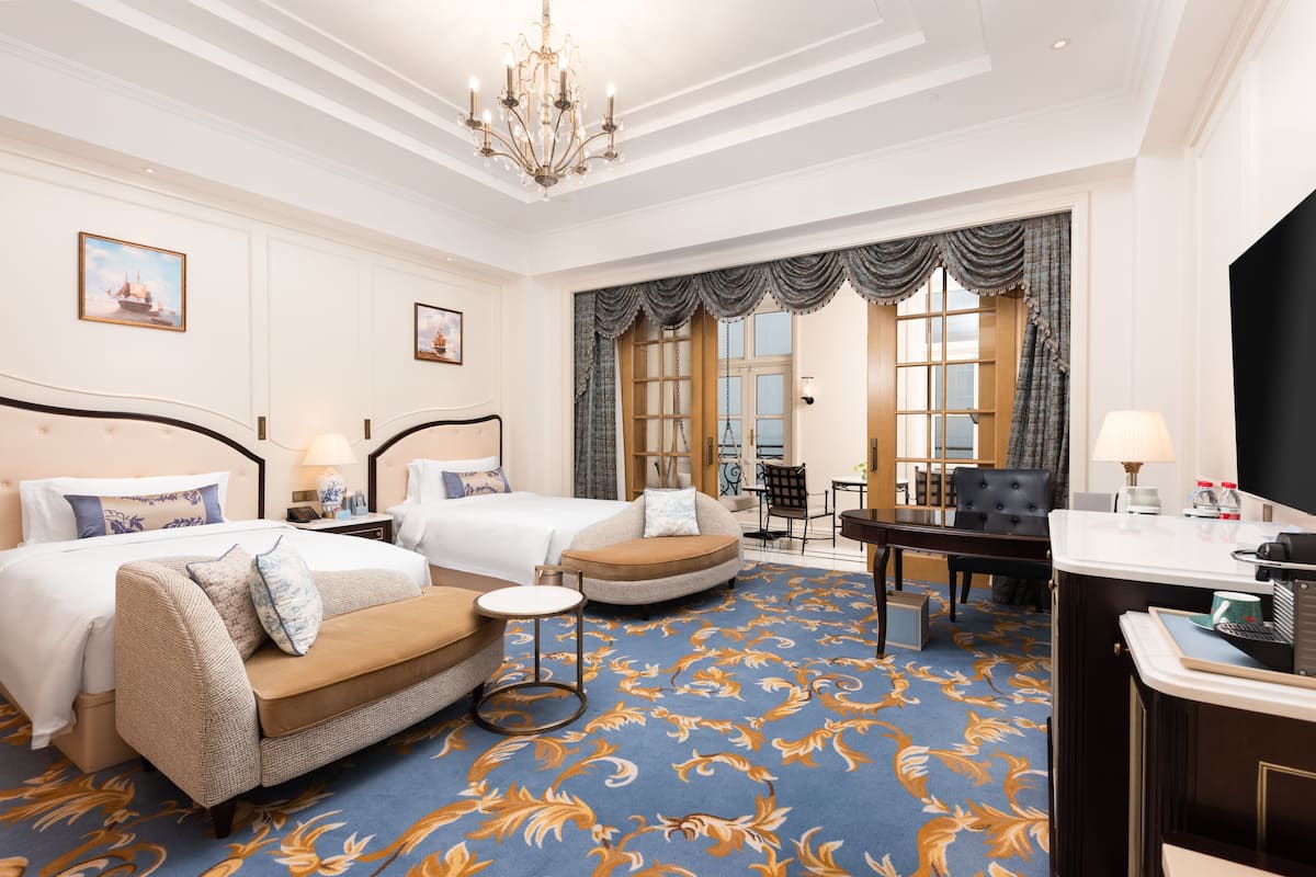 A hotel room with two beds, a sofa, a round table, and a desk with a lamp.