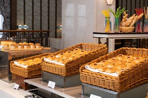 Una exhibición de pastelería con productos horneados en cestas de mimbre, una mesa con pan y aderezos, y un fondo de papel tapiz con motivos florales.