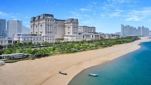 Un paisaje urbano costero con un edificio histórico destacado, una playa arenosa y un mar tranquilo.