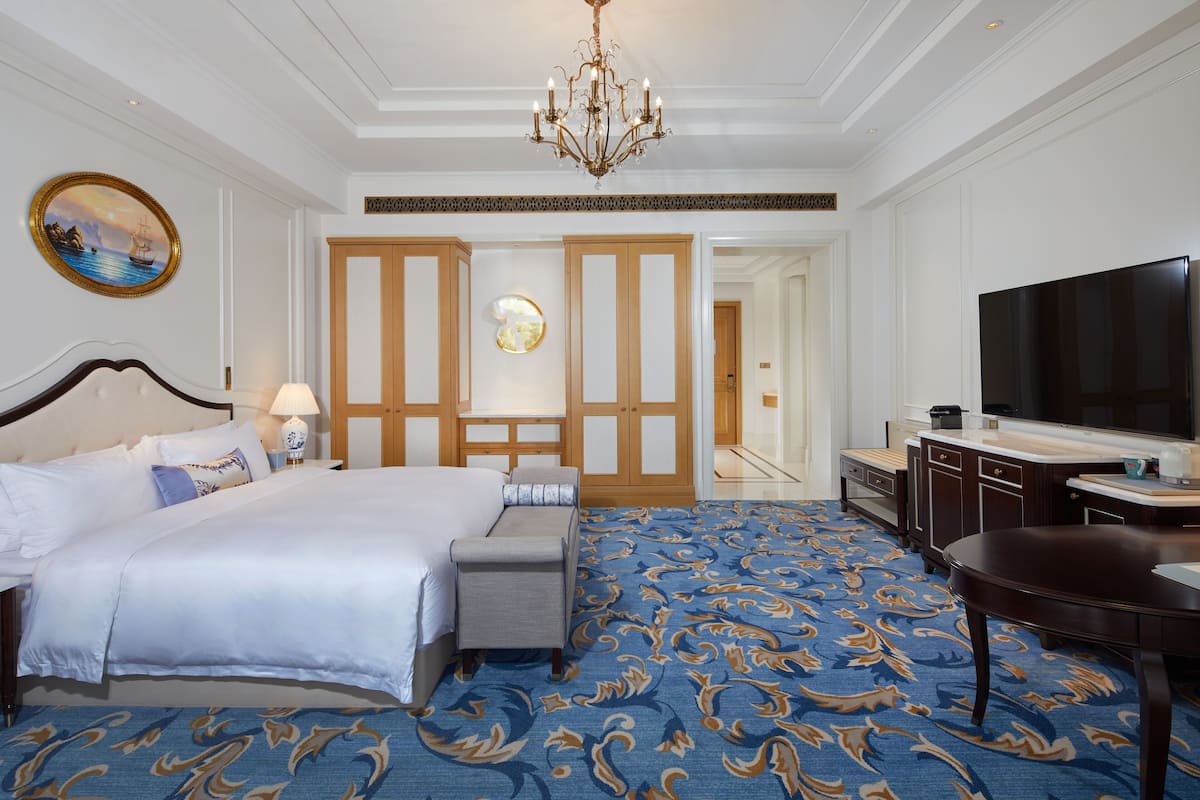 A hotel room with a large bed, a TV, a desk, and a bathroom visible through an open door.