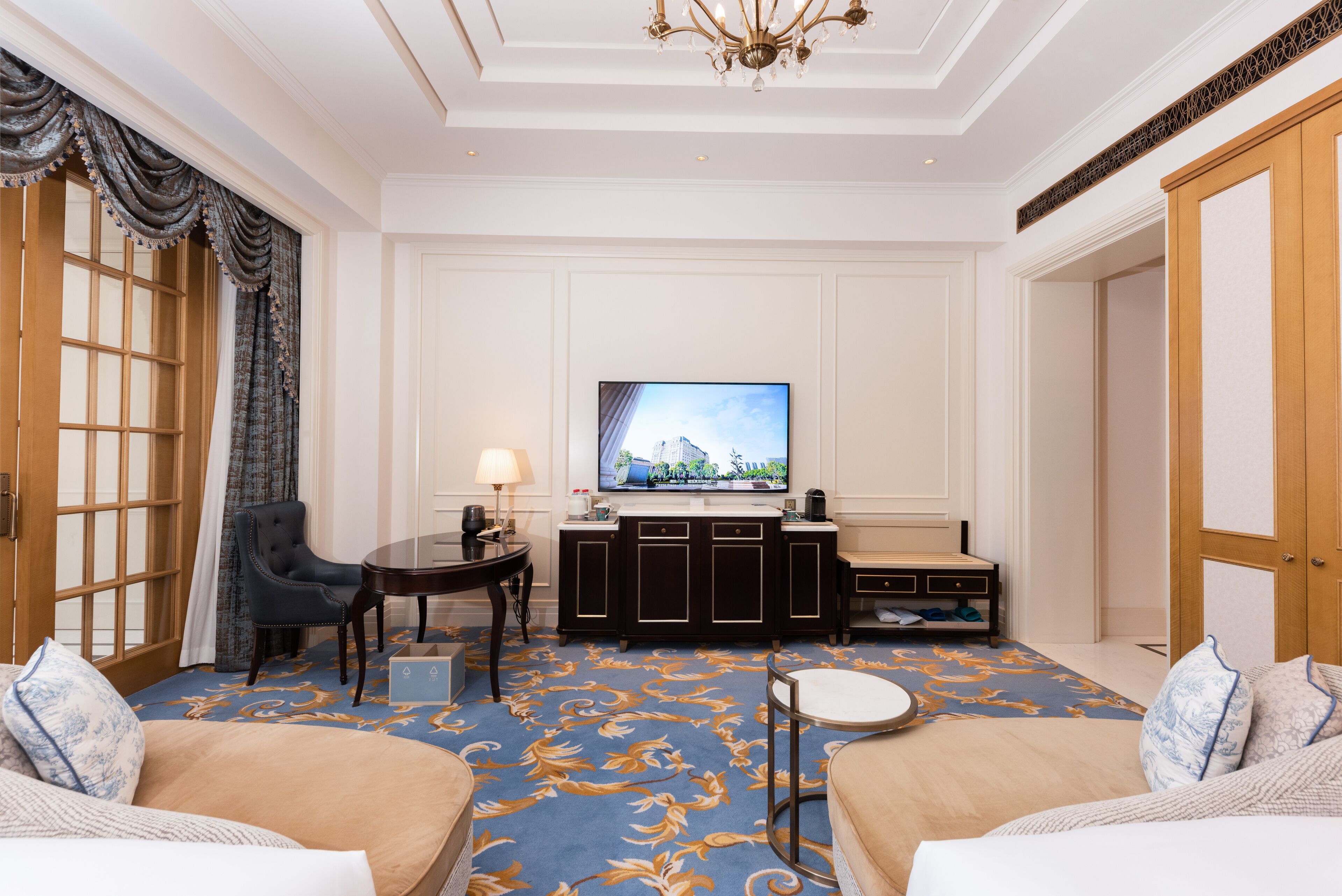 A hotel room with a large flat-screen TV, a sofa, a chair, a small table, and a cabinet.