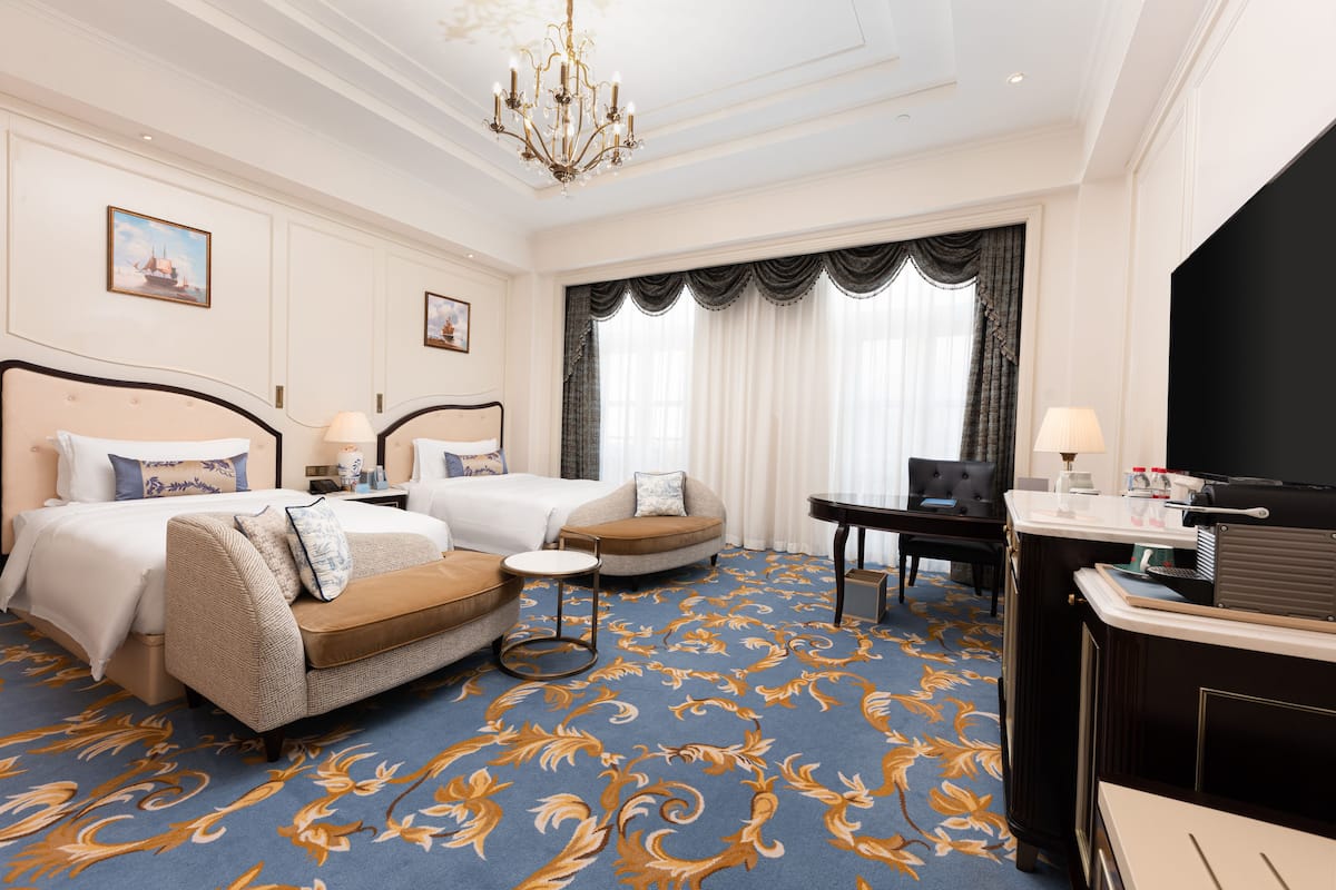 A hotel room with a large bed, two sofas, a desk, and a chandelier.