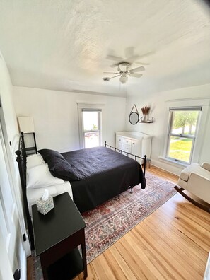 Une chambre à coucher comprenant un lit, une table de chevet, une commode et un ventilateur de plafond.