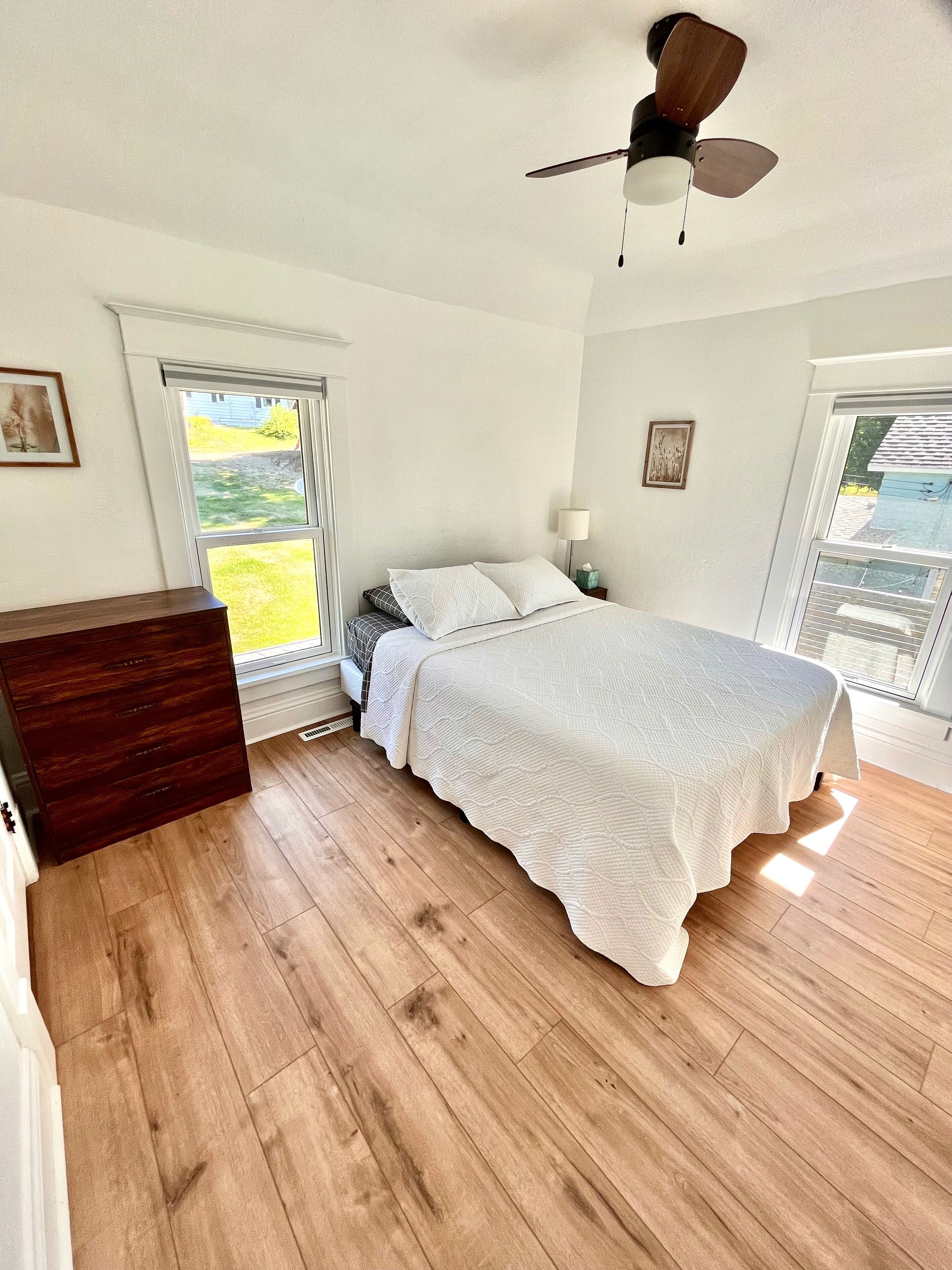 Ein Schlafzimmer mit Bett, Holzboden, Deckenventilator und großen Fenstern.