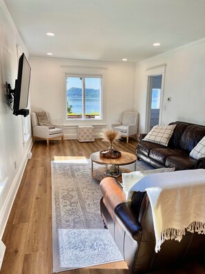 Un salon moderne avec vue sur la mer, comprenant un canapé en cuir, deux fauteuils, une table basse et un téléviseur fixé au mur.