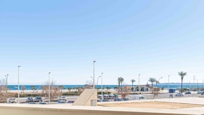 Vista d'un aparcament ple de cotxes, palmeres i una platja al fons.