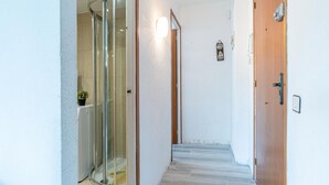 Un couloir avec une douche en verre, une porte en bois et une petite plante en pot.