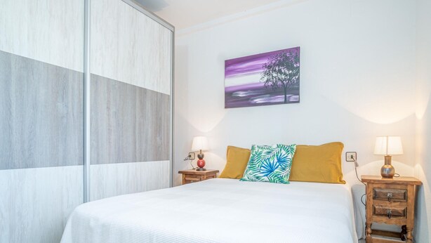 Une chambre à coucher comprenant un lit, deux tables de chevet, une commode, un tableau accroché au mur et une porte coulissante.