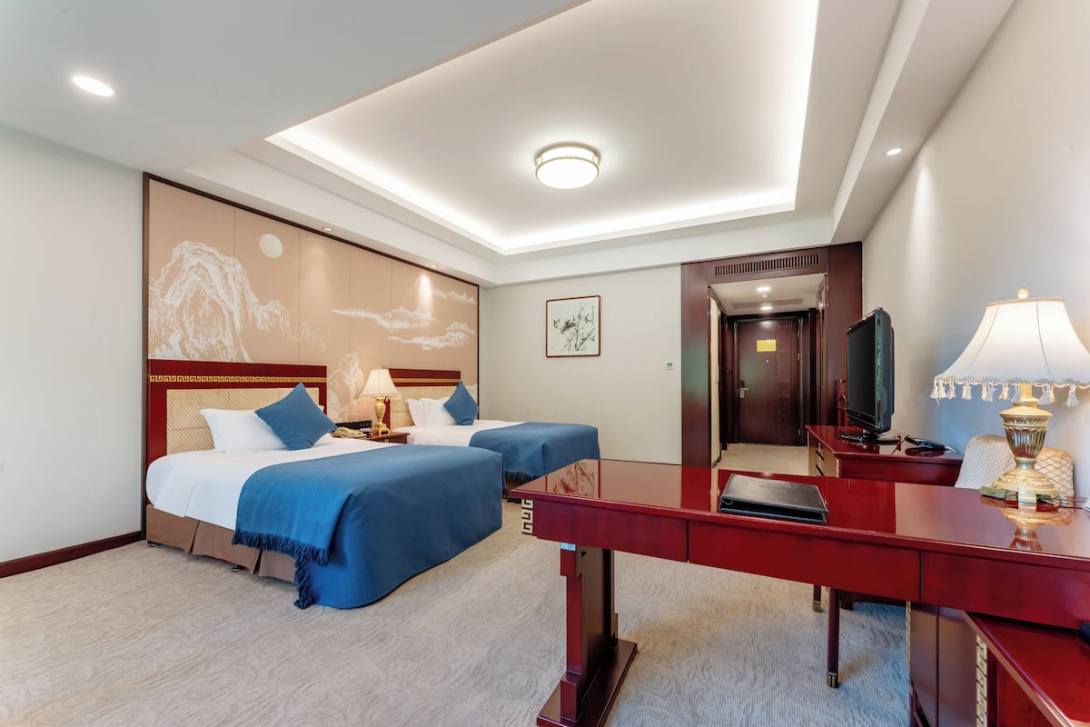 A hotel room with two beds, a desk, a television, and a lamp.