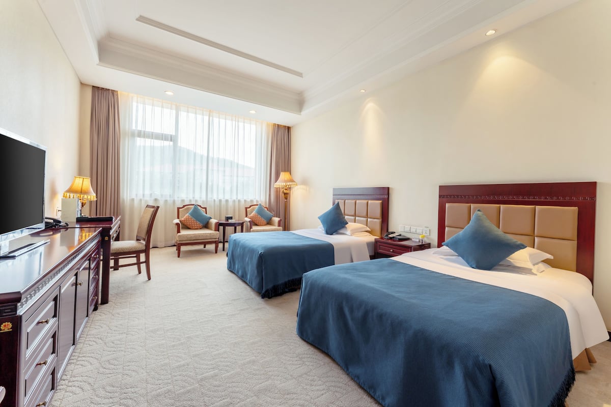 A hotel room with two beds, a TV, a desk, and a chair.