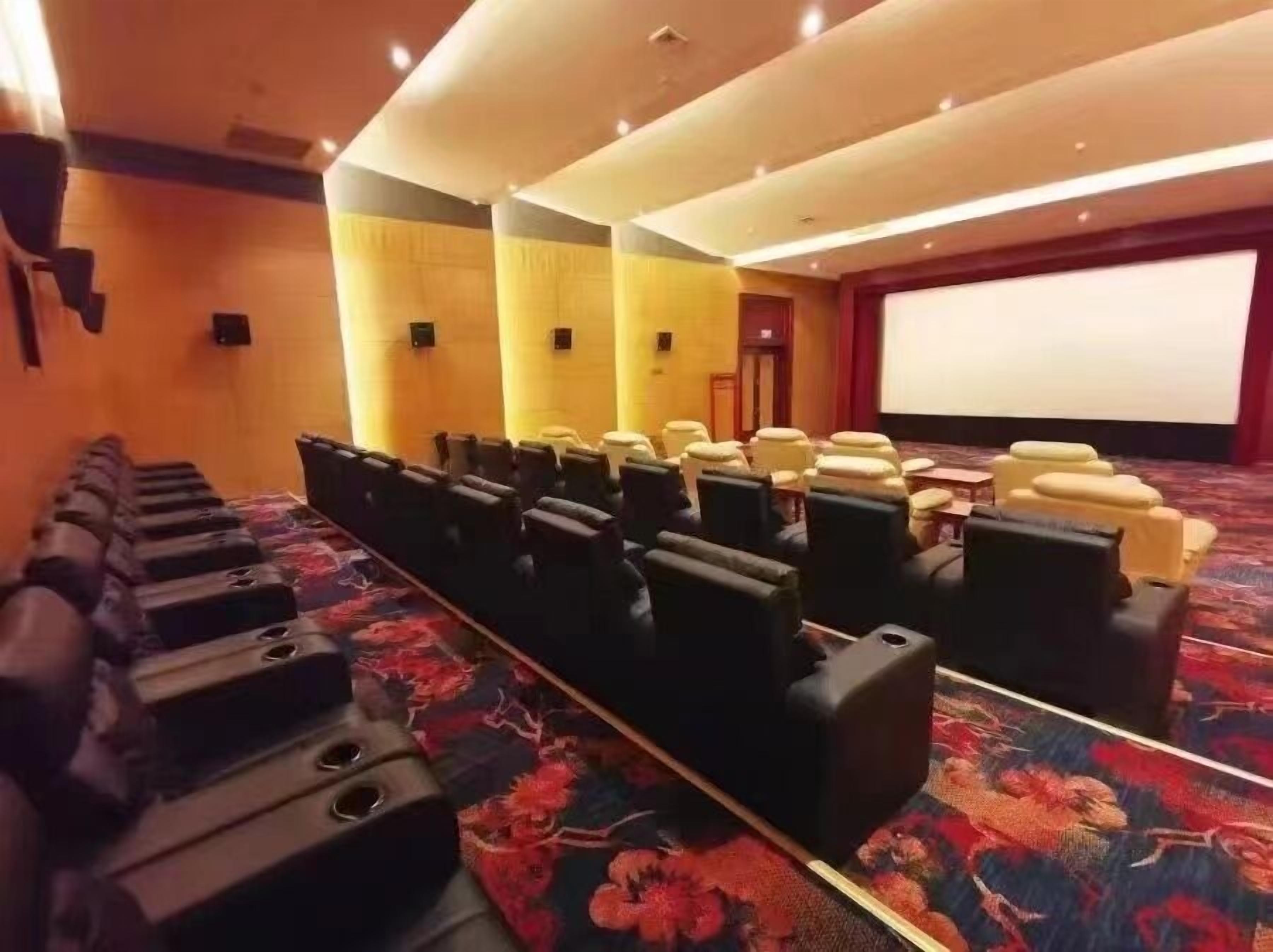 A theater with rows of black seats, a large screen, and a carpeted floor.