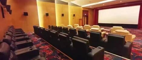 A theater with rows of black seats, a large screen, and a carpeted floor.