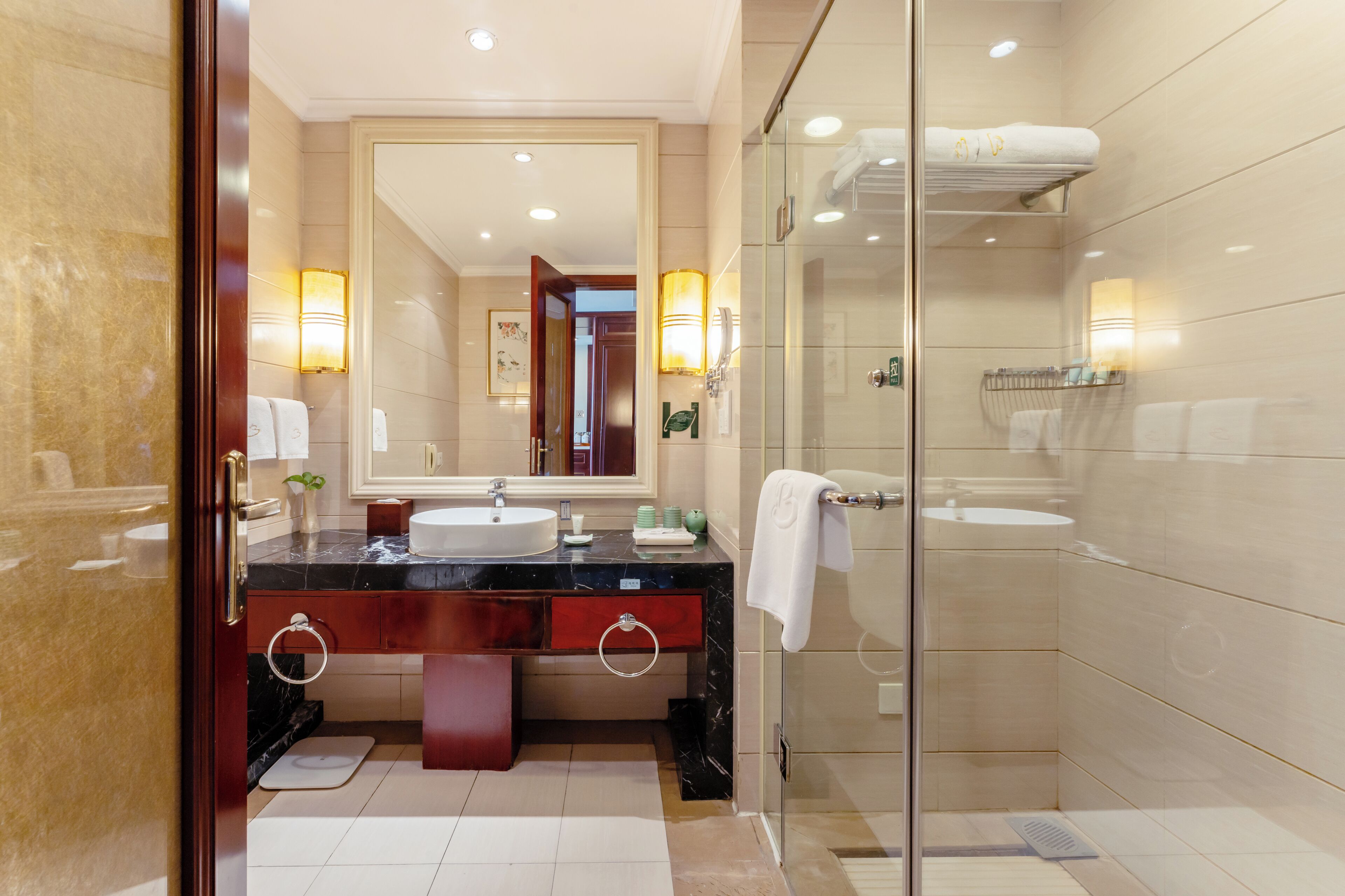 A modern bathroom with a marble vanity, a large mirror, a glass shower enclosure, and a towel rack.