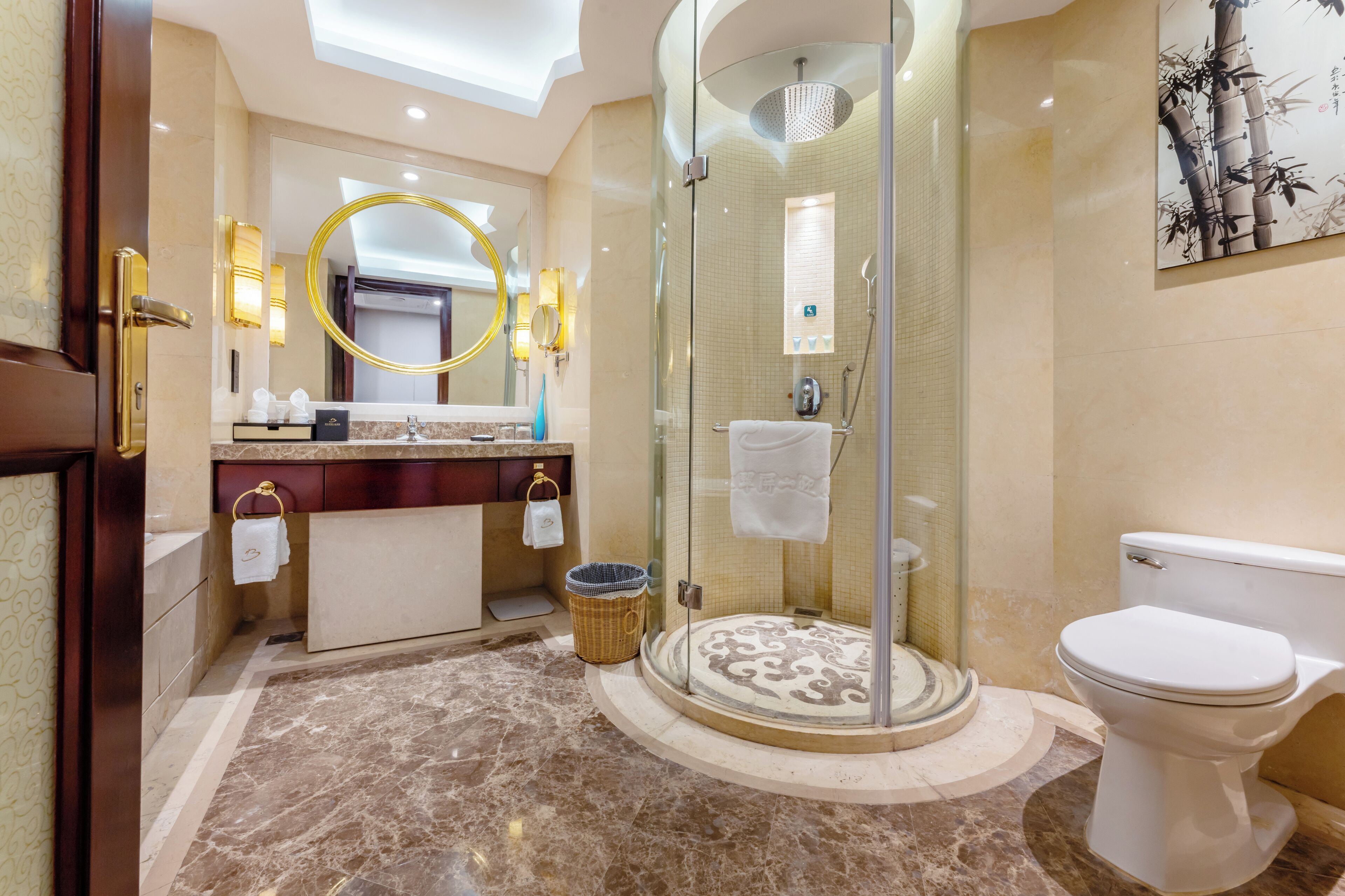 A modern bathroom with a glass-enclosed shower, a round mirror, a toilet, and a vanity with a towel rack.