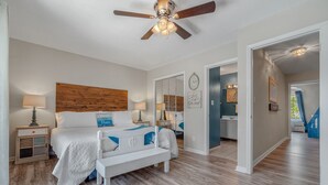 A bedroom with a bed, bedside tables, a ceiling fan, and a bathroom visible through an open door. - Beachy Charm 2BR | Walk to Beach + Parking (Miramar Beach)