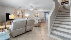 A spacious living room with a sofa, a TV, and a dining area with chairs. - Beachy Charm 2BR | Walk to Beach + Parking (Miramar Beach)