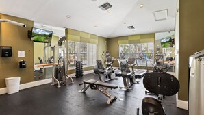 Ein Fitnessstudio mit verschiedenen Trainingsgeräten, großen Fenstern und einem Spiegel, der die Geräte reflektiert.