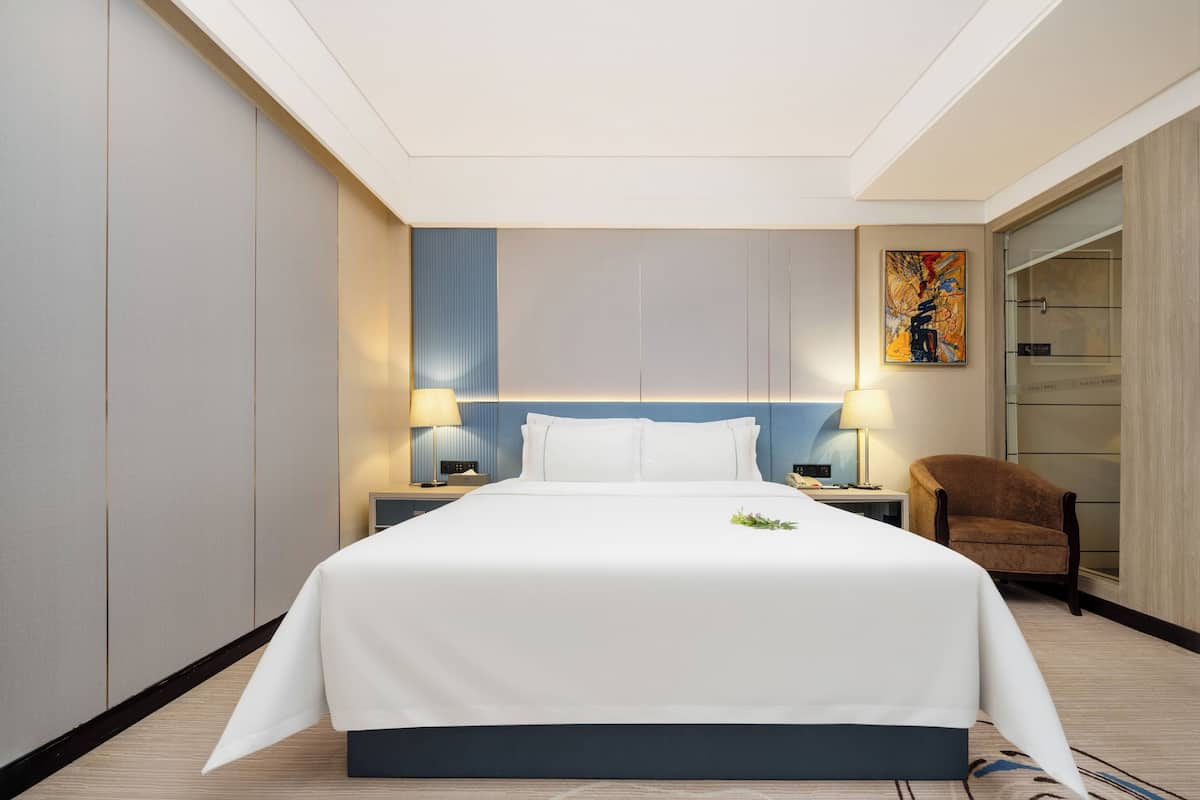 Ein Hotelzimmer mit einem großen Bett, zwei Nachttischen mit Lampen, einem Sessel und einem Bild an der Wand.