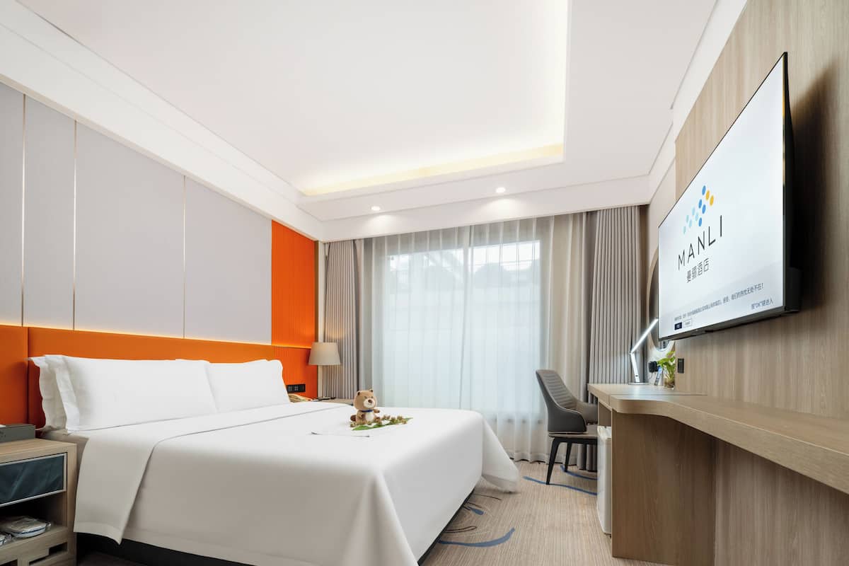 Ein Hotelzimmer mit einem großen Bett, einem Schreibtisch, einem Stuhl und einem Fernseher, der den Namen des Hotels zeigt.