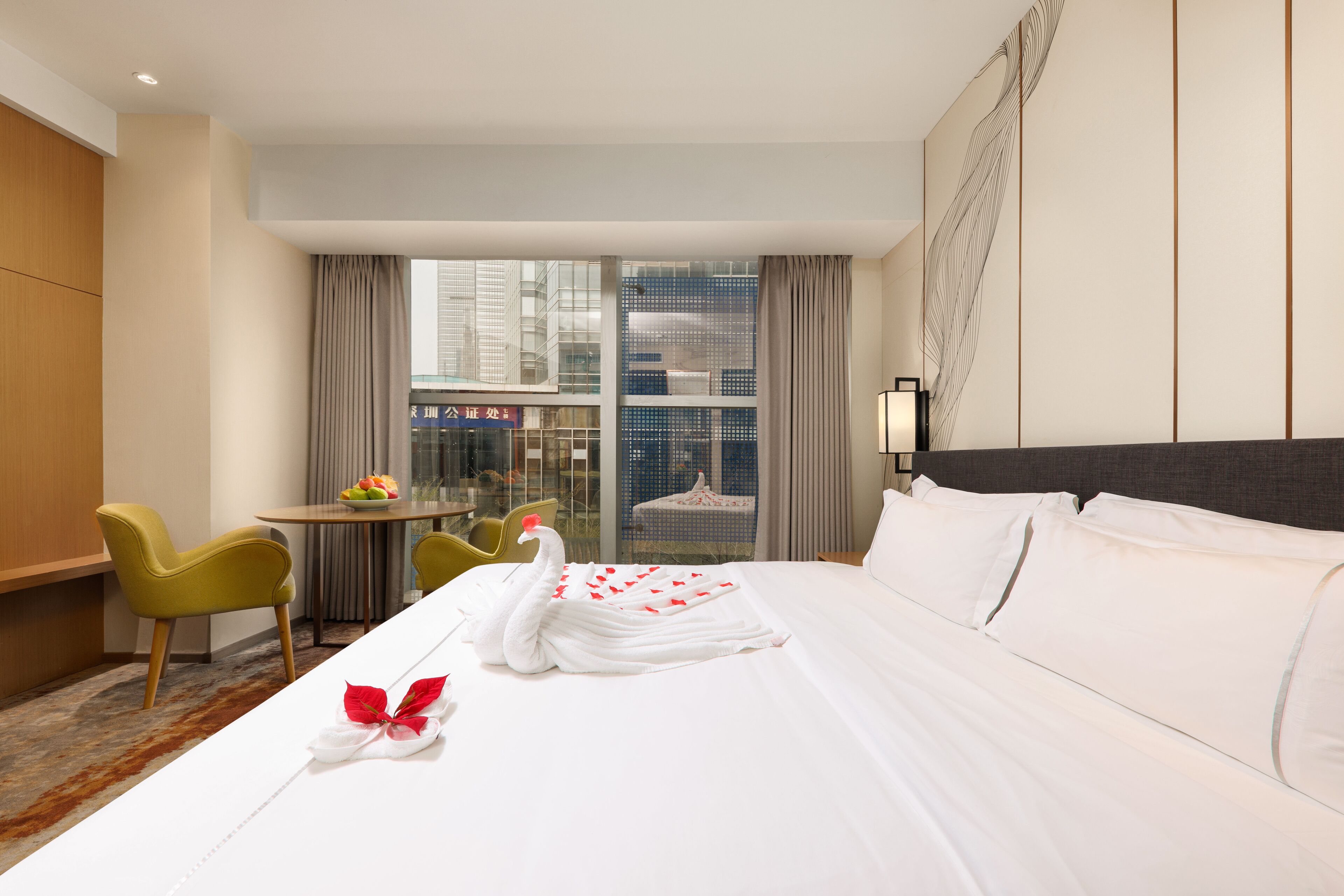 A hotel room with a large bed, a dining table, two chairs, and a view of the cityscape through the window.