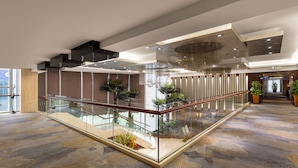 Eine großzügige Lobby mit einer Glaskonstruktion als Treppe, modernen Leuchten und Zimmerpflanzen.