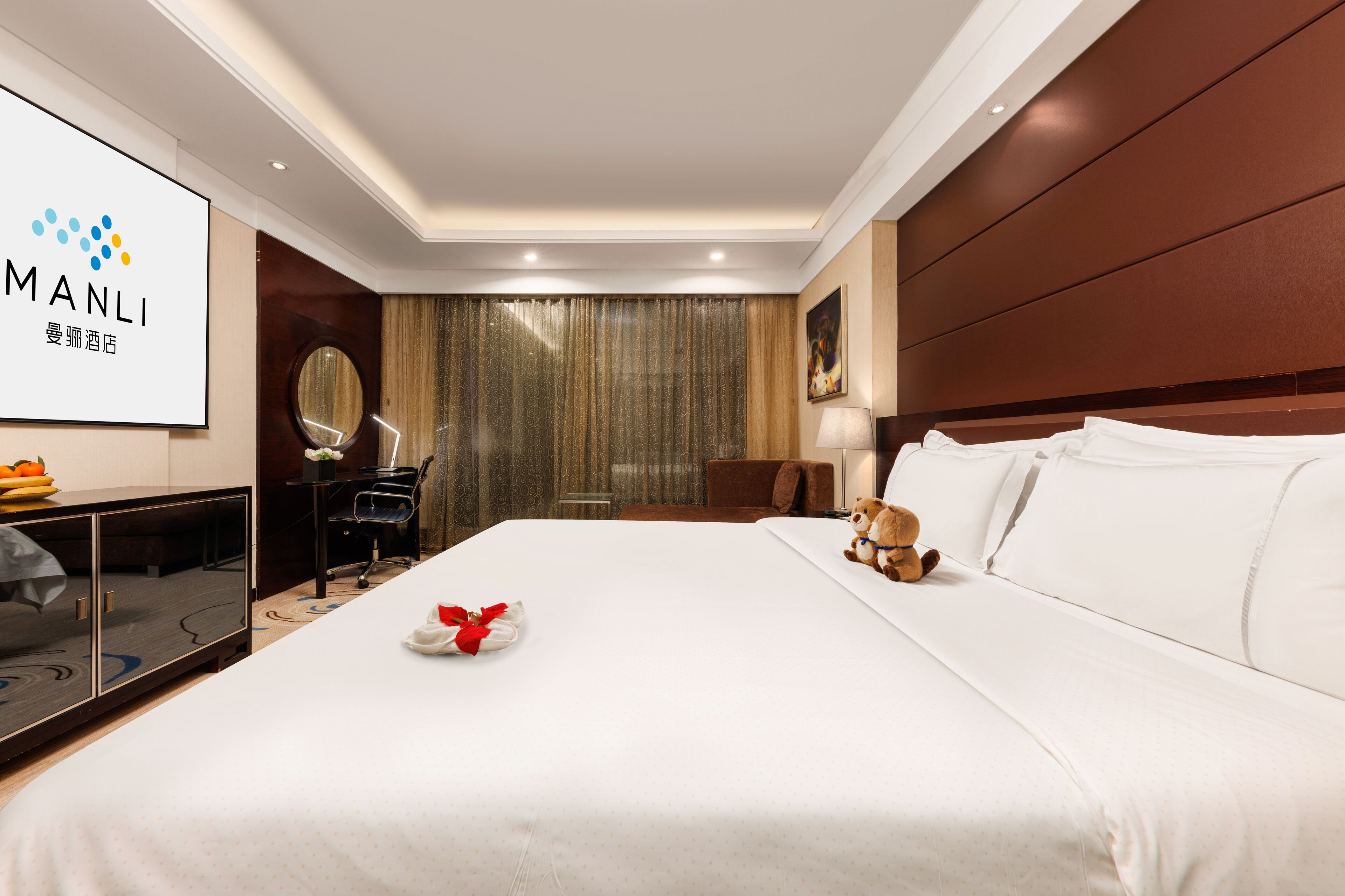 A hotel room with a large bed, a desk with a computer, a TV, and a wall-mounted mirror.