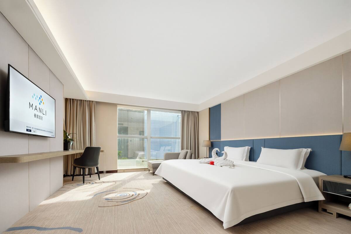 Ein modernes Hotelzimmer mit einem großen Bett, einem Flachbildfernseher an der Wand, einem Schreibtisch und einem Sessel.