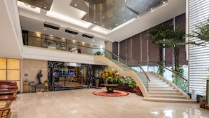 Eine großzügige Lobby mit Marmorboden, einer zentralen Blumenkomposition, einer Treppe und einem Empfangsschalter.