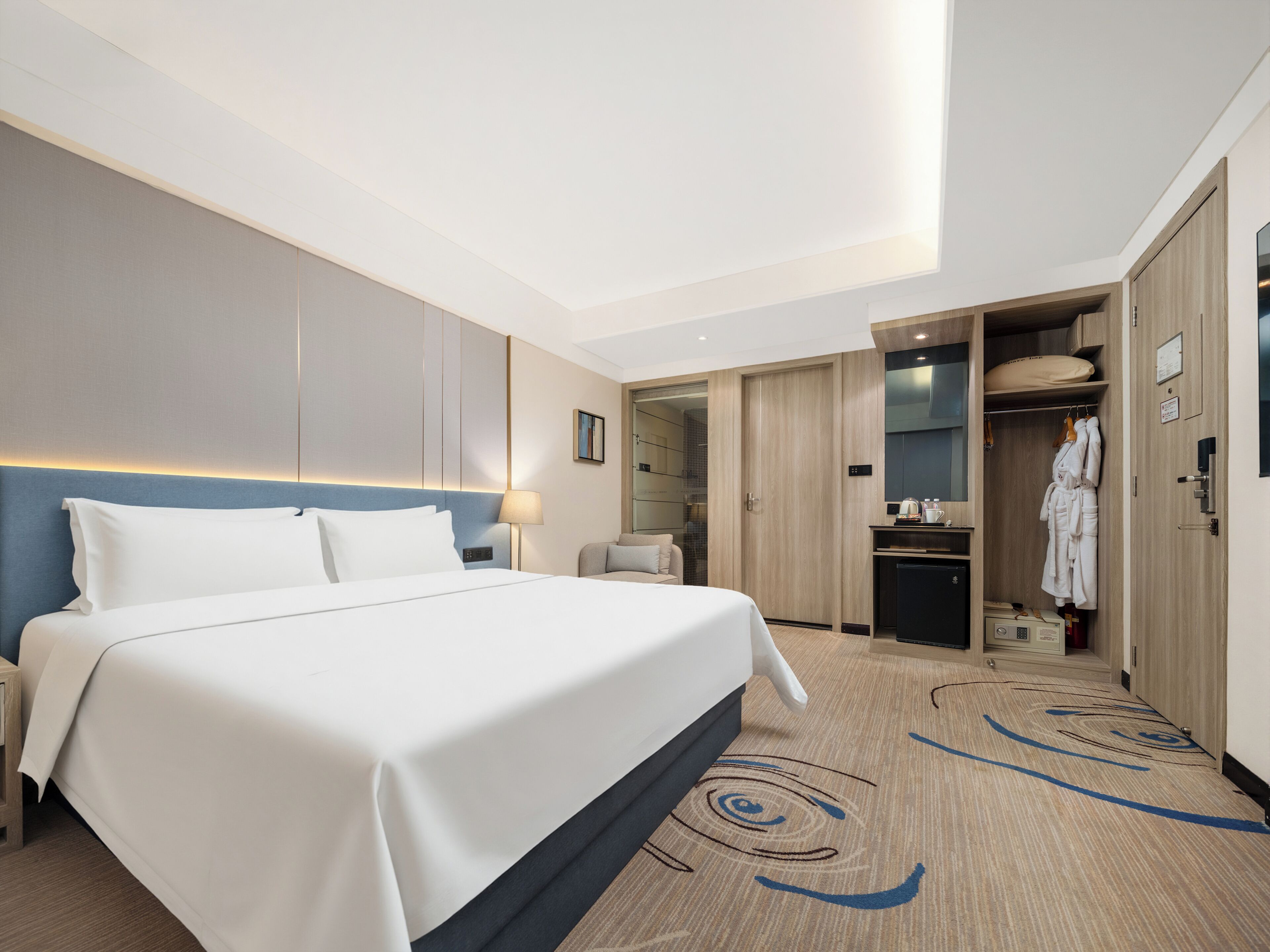 A modern hotel room with a large bed, a desk, a chair, a wardrobe, and a bathroom.