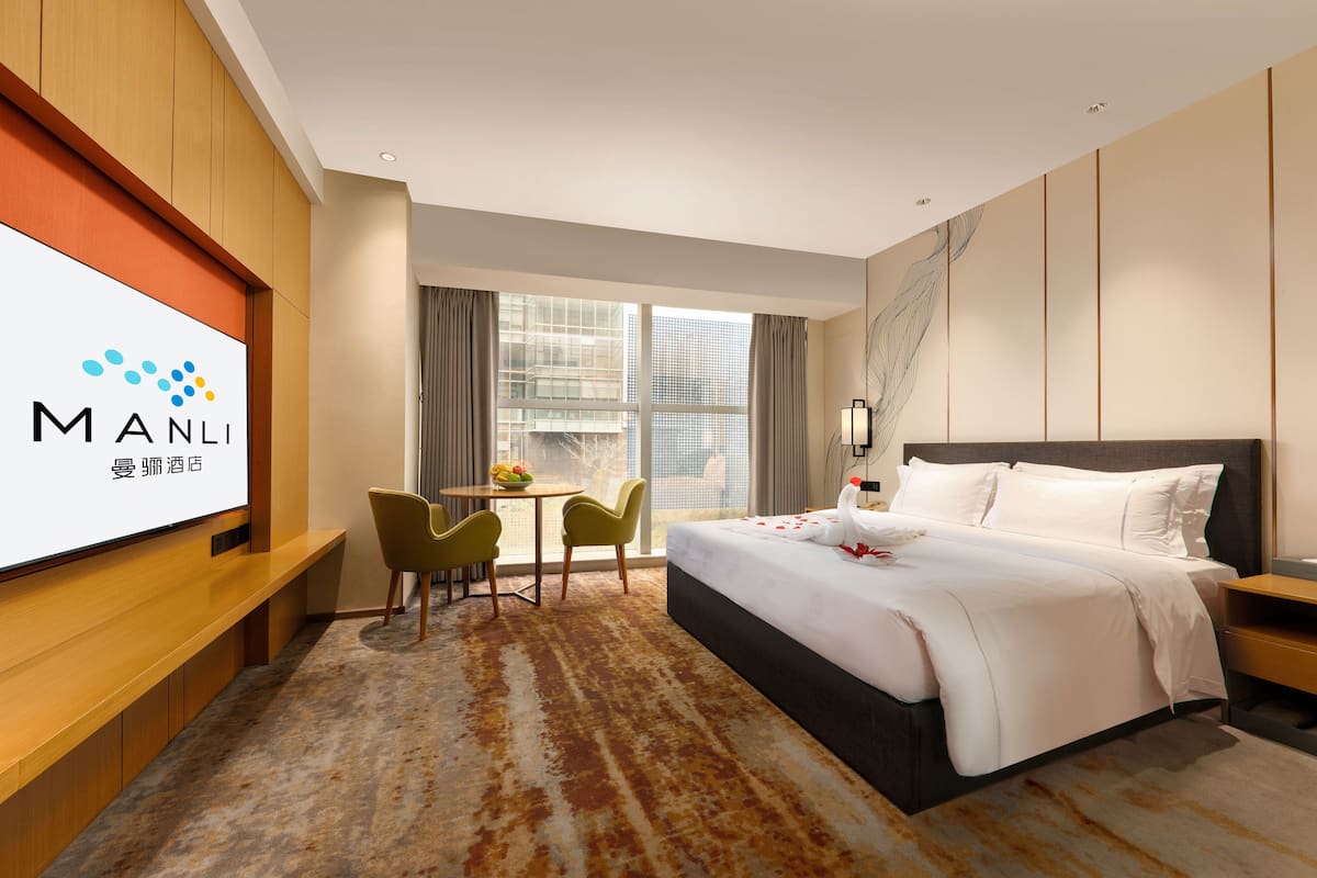 Ein Hotelzimmer mit einem Bett, einem Schreibtisch, zwei Stühlen, einem Fernseher und einem Fenster mit Vorhängen.