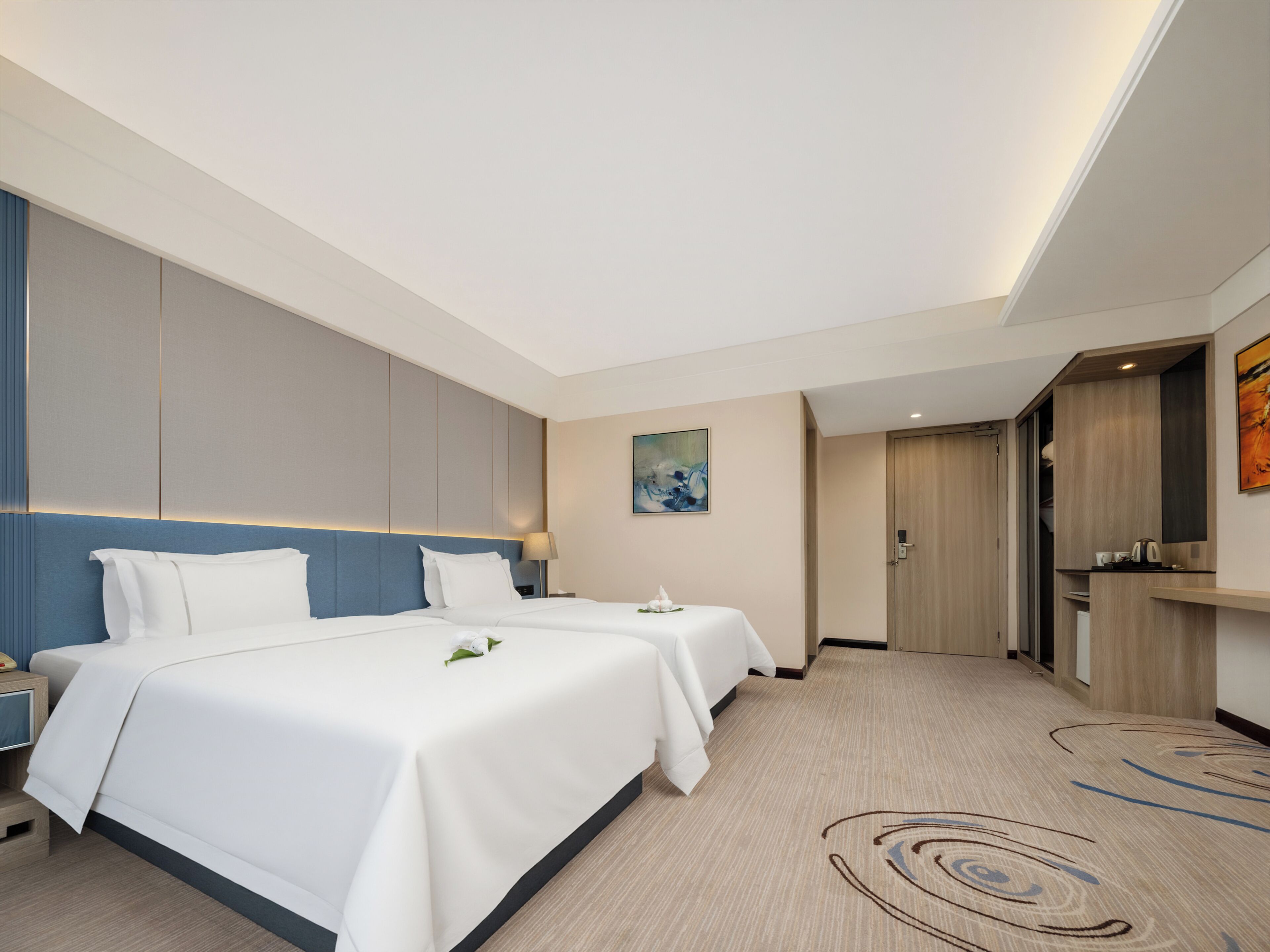 Une chambre d’hôtel avec deux lits, un bureau, une chaise, un tableau et une porte donnant sur une salle de bain.