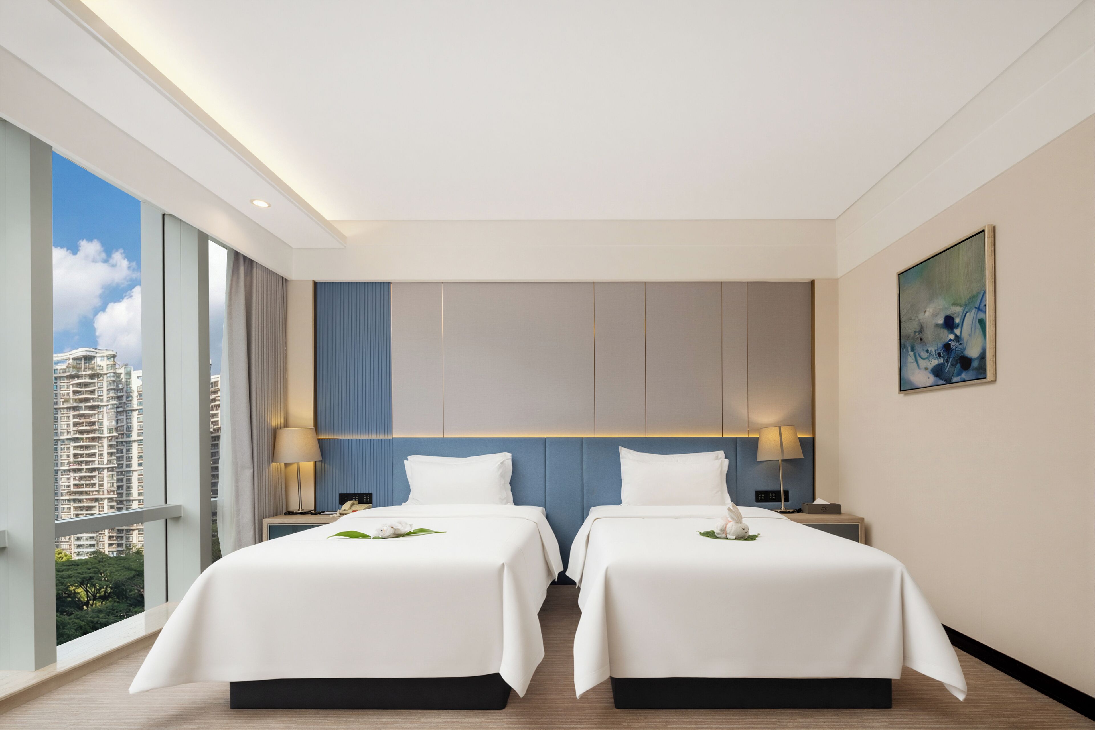 Ein Hotelzimmer mit zwei Betten, Blick auf die Stadt und einem Bild an der Wand.