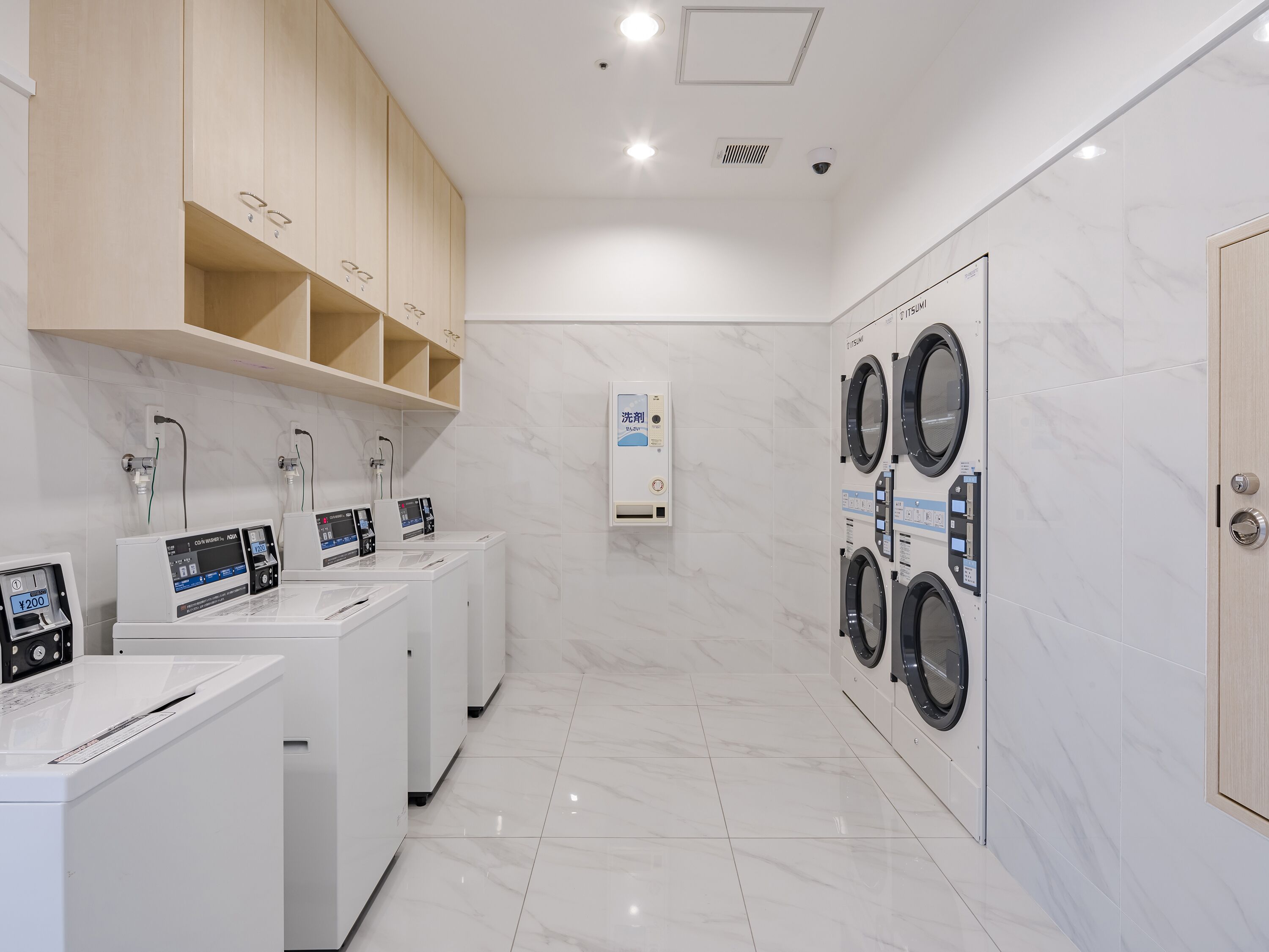 A modern laundry facility with multiple washing machines and dryers, a control panel, and a water heater.