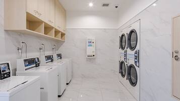 A modern laundry facility with multiple washing machines and dryers, a control panel, and a water heater.