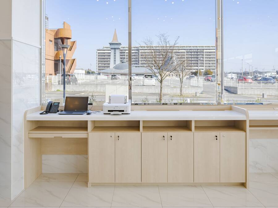 A modern office desk with a laptop, phone, and printer, large windows with a city view, and a clean, minimalist design.