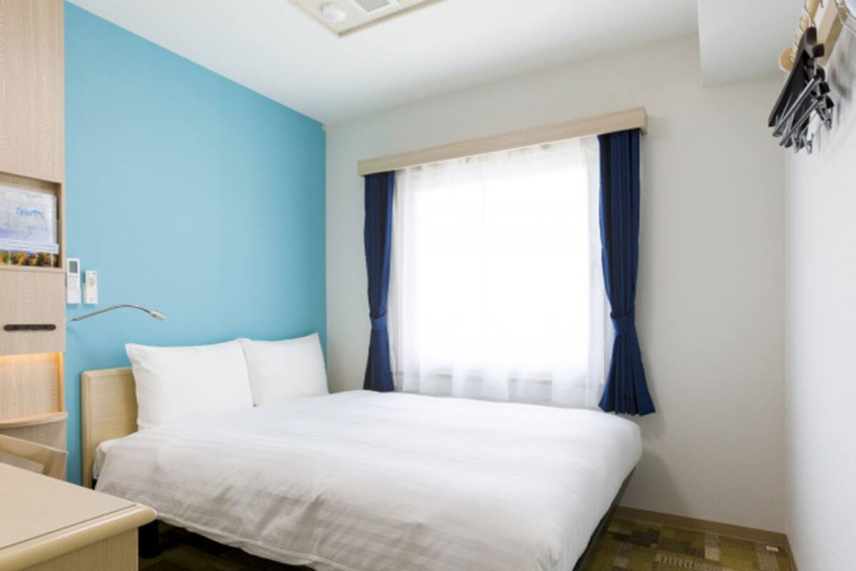 A hotel room with a bed, a desk, a chair, a wardrobe, and a window with curtains.