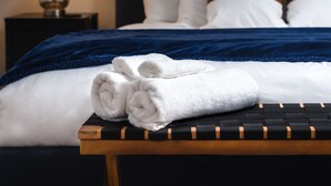 Ein ordentlich bezogenes Bett mit weißer und blauer Bettwäsche, ein Nachttisch aus Holz mit Handtüchern, einer Lampe und einem Bilderrahmen mit einem Pferdebild an der Wand.