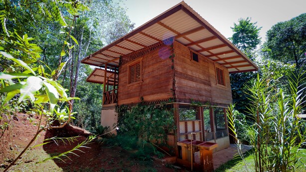 Una estructura de madera con techo inclinado y un balcón, rodeada de abundante vegetación.