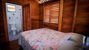 Una habitación estilo cabaña de madera, con cama, inodoro y ventana con persianas.