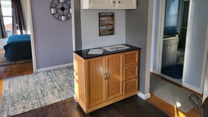 A compact kitchen with wooden cabinets, a black countertop, and a decorative backsplash. - Park Place-Quaint home nestled between parks and lakes (Olney)