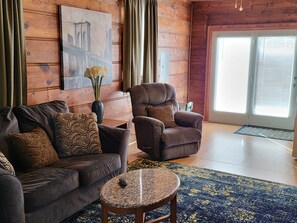 Un salon chaleureux avec un canapé en cuir marron, un fauteuil marron, une petite table ronde et un tapis bleu à motifs.