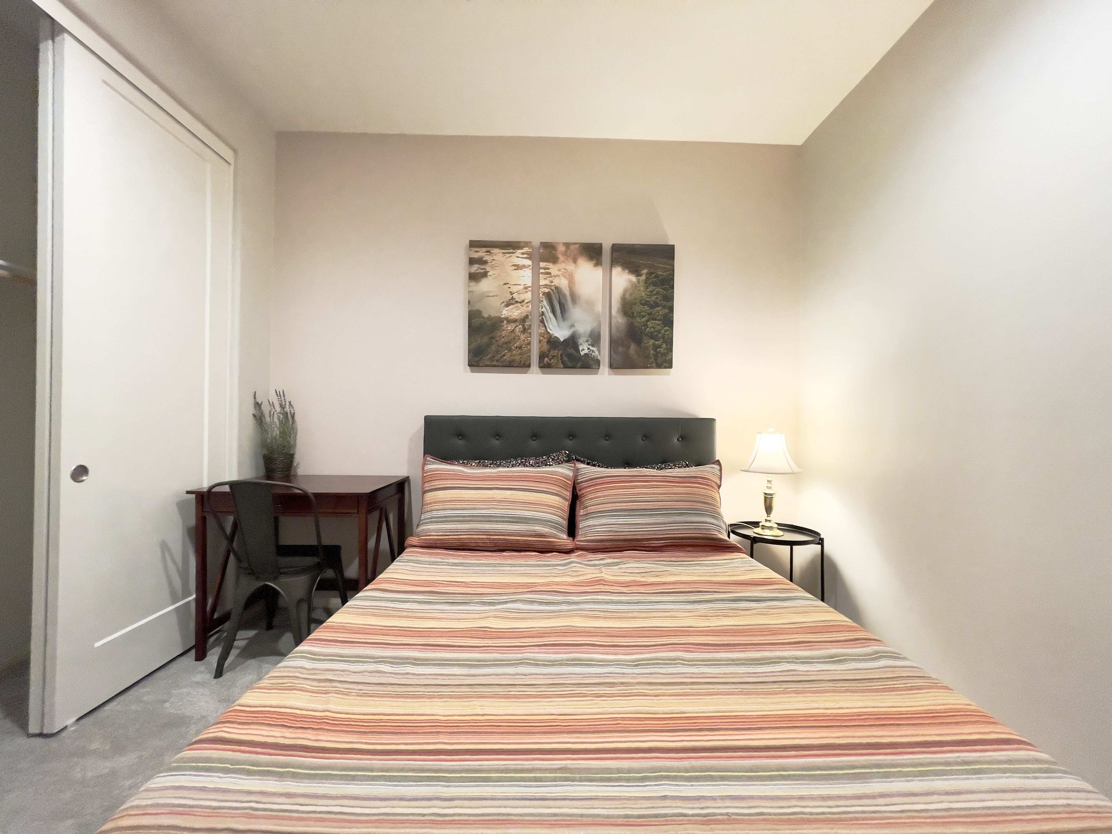 Une chambre à coucher avec un lit, un bureau et une chaise. Deux cadres avec des photos sont accrochés au mur au-dessus du lit.