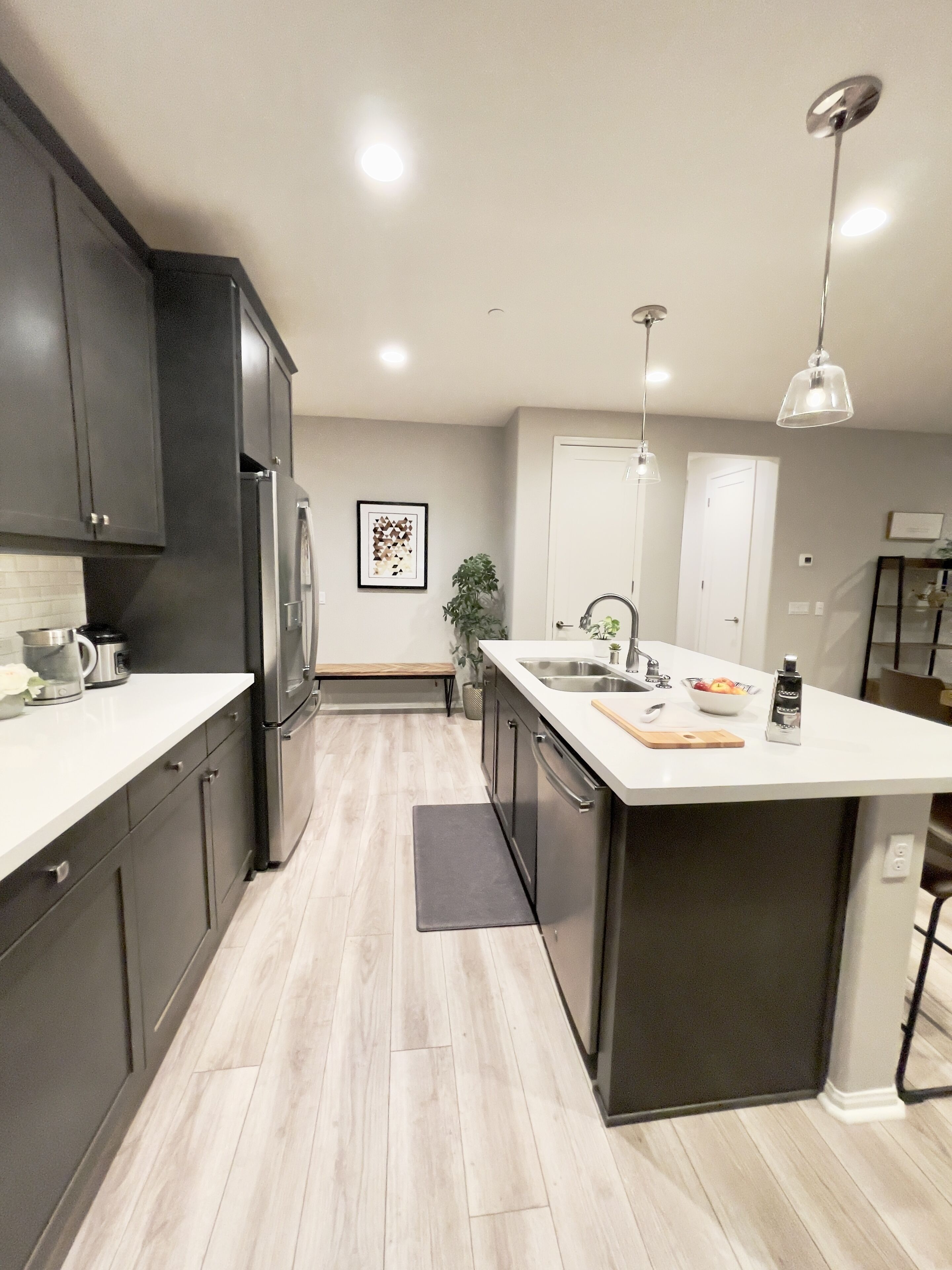A modern kitchen with dark cabinets, a large island, stainless steel appliances, and a minimalist design.
